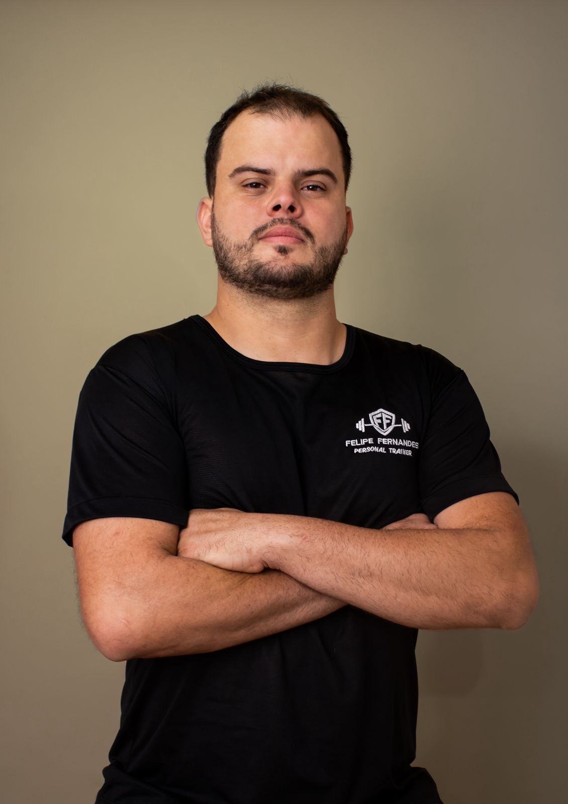 Felipe Fernandes, personal trainer, de braços cruzados com camiseta preta da marca